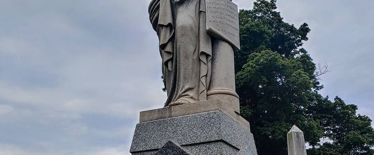 A statue of a woman in a park with gravestones in the background.