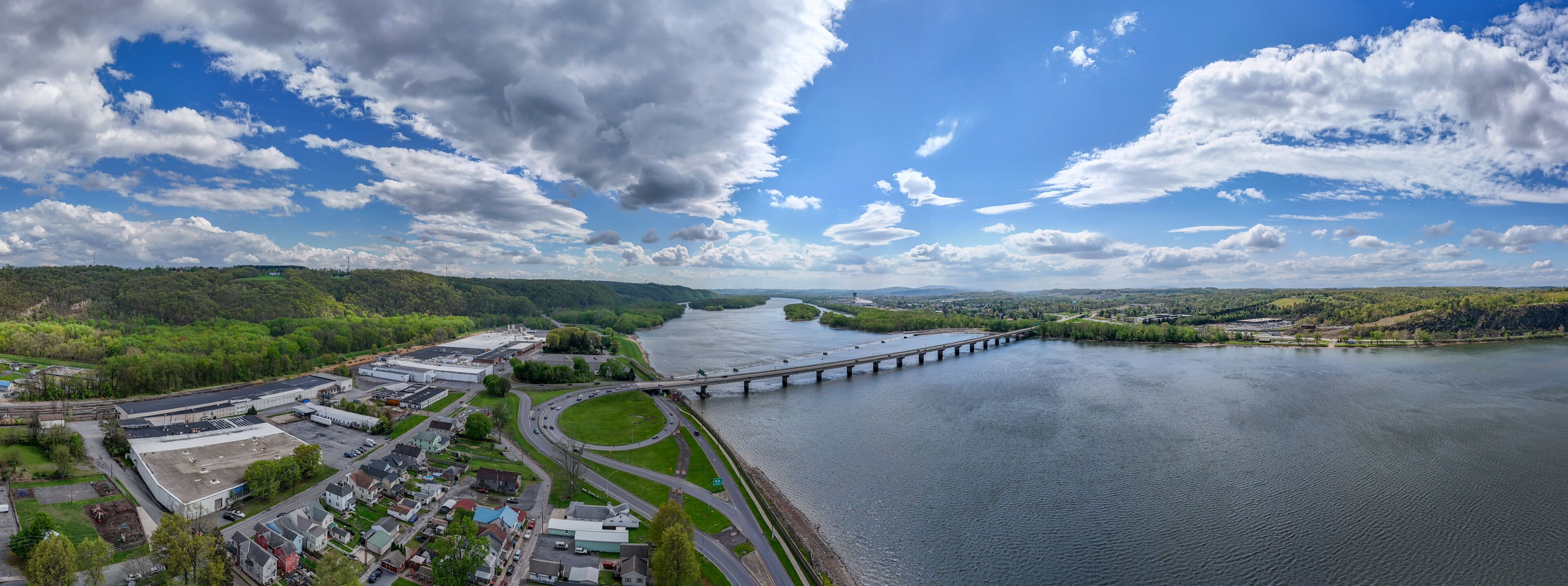 A river with a bridge, industrial buildings, and a green landscape.
