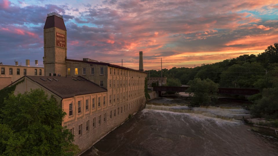 A historic industrial building with a tall chimney and a river flowing beside it.
