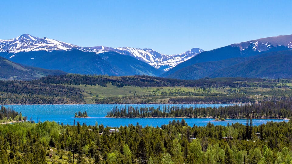 A mountainous landscape with a lake surrounded by dense forests and snow-capped peaks.