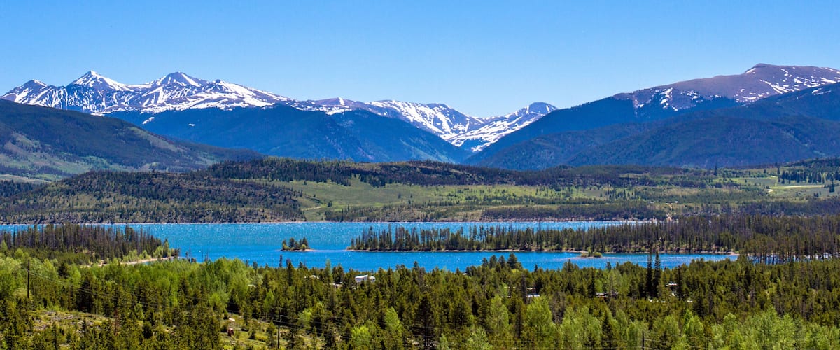 A mountainous landscape with a lake surrounded by dense forests and snow-capped peaks.