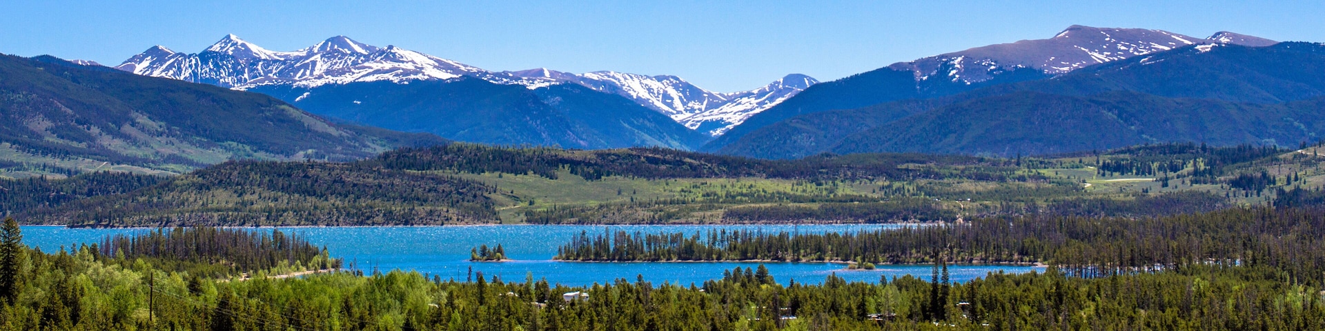 A mountainous landscape with a lake surrounded by dense forests and snow-capped peaks.