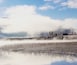 A misty landscape with a calm body of water reflecting the sky and vegetation.