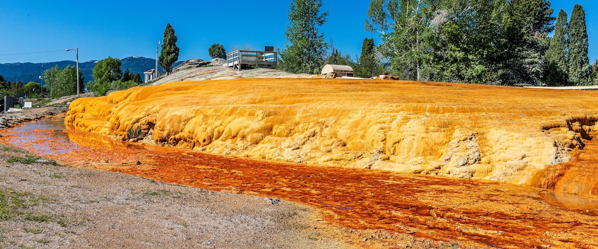 A geothermal area with orange mineral deposits, a wooden structure, and trees.