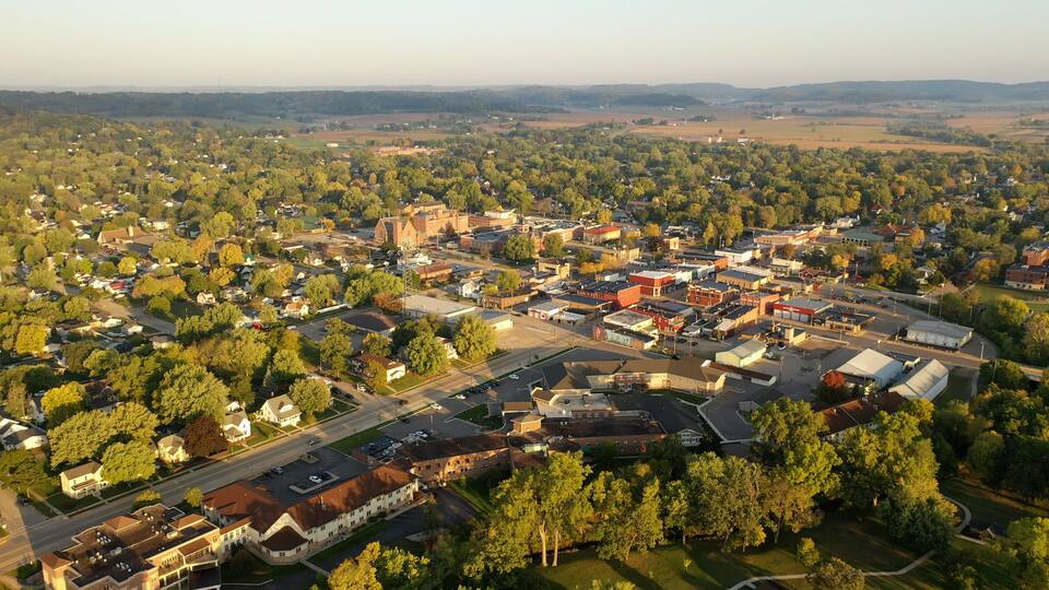 An aerial view of a small town with dense tree coverage, a central church, and a mix of residential and commercial buildings.