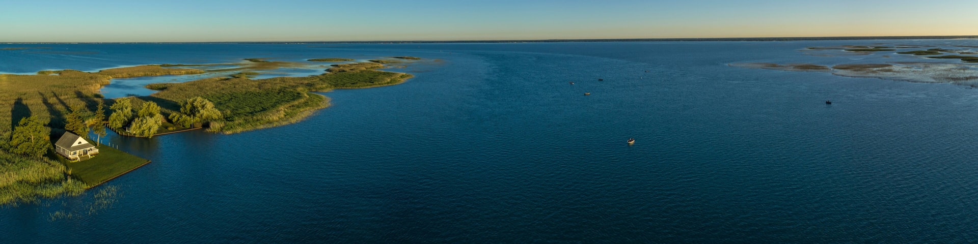 A coastal landscape with a house on a small island, surrounded by water and vegetation.