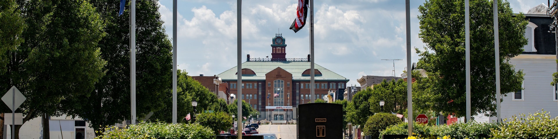 A flag display with multiple flags, a building in the background, and benches in a park.