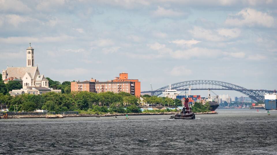 A river with a sailboat, a bridge, and buildings including a church.