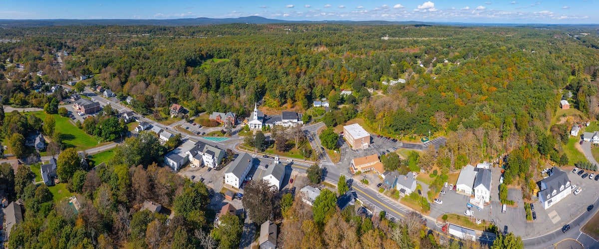 An aerial view of a town surrounded by dense forests, with a mix of residential and commercial buildings, and a prominent church.