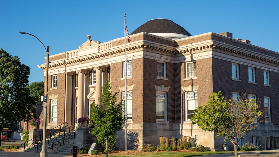 A historic brick building with a dome and columns, surrounded by trees and a clear blue sky.