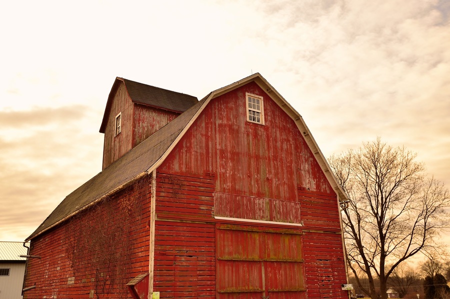 An old, weathered red barn sitting among barren trees below a winter sky in northeastern Illinois. The barn's style and architecture are , fairly typical of those found in the Midwest United States.