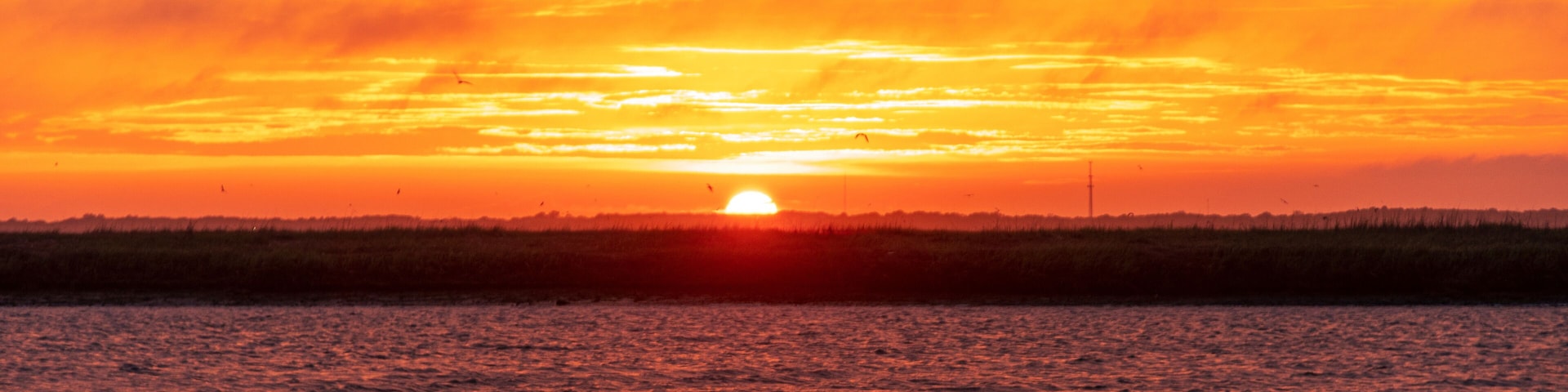 A sunset over a body of water with a horizon line and a distant landmass.
