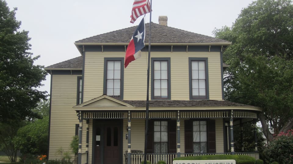 A historic building with a Texan flag and a Texas state flag, labeled as the Moody Museum.