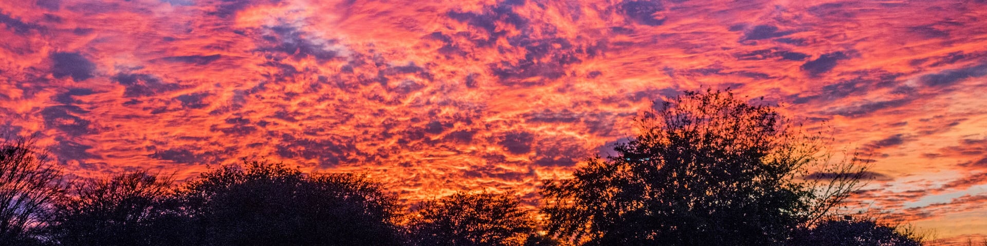 A sunset sky with vibrant pink and purple clouds over a silhouetted landscape.