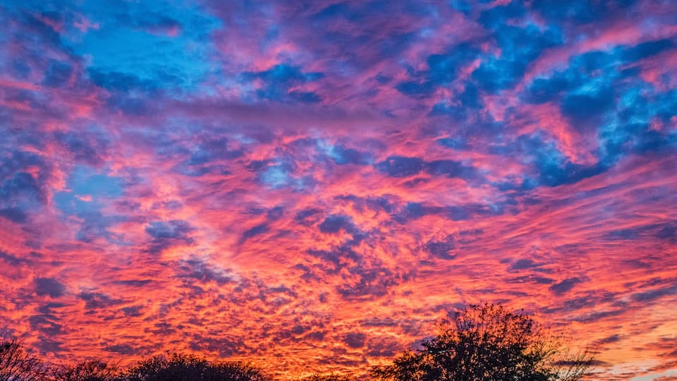 A sunset sky with vibrant pink and purple clouds over a silhouetted landscape.