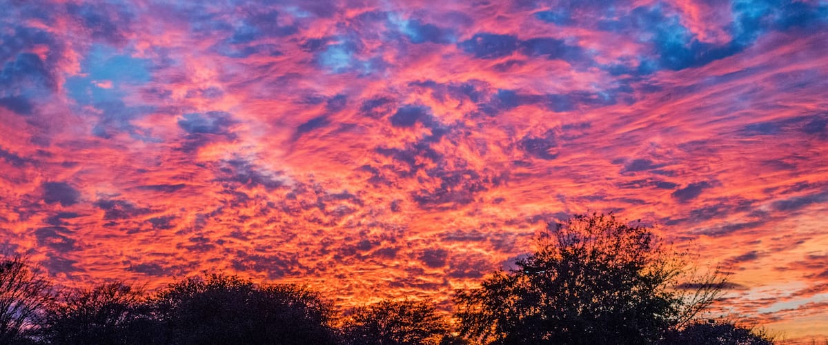 A sunset sky with vibrant pink and purple clouds over a silhouetted landscape.