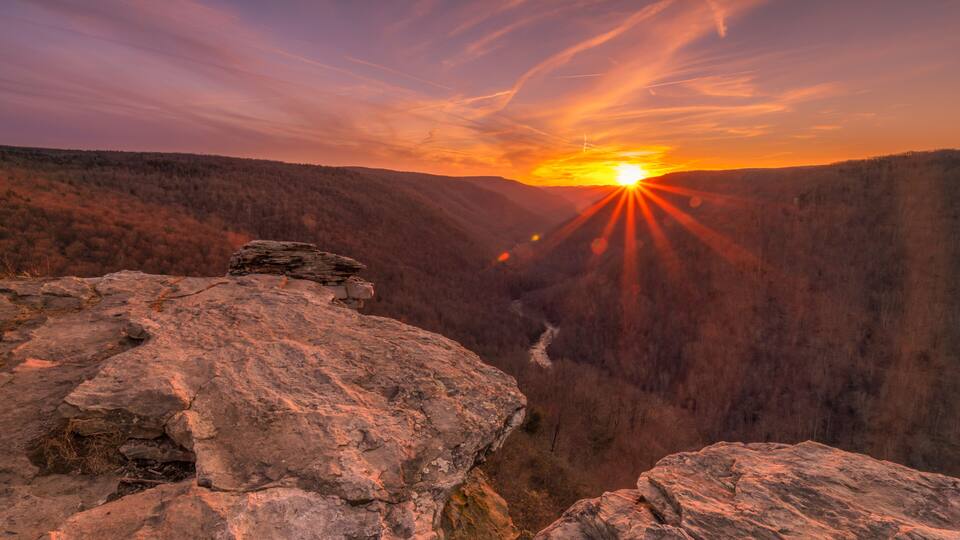 A sunset over a canyon with rocky terrain and a river.
