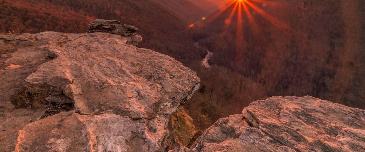 A sunset over a canyon with rocky terrain and a river.