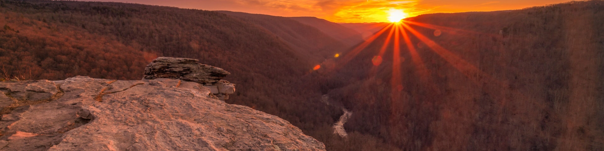 A sunset over a canyon with rocky terrain and a river.