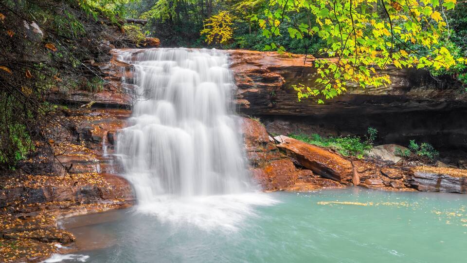 A waterfall cascading over rocky terrain surrounded by autumn foliage.
