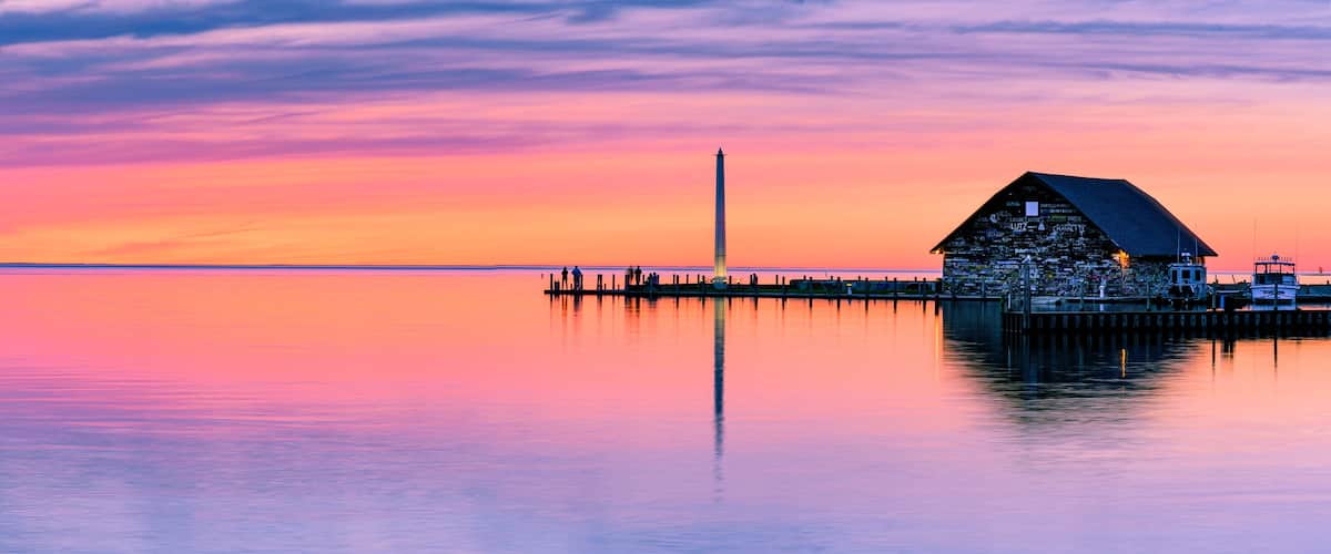 A lighthouse at sunset with a colorful sky and calm water.