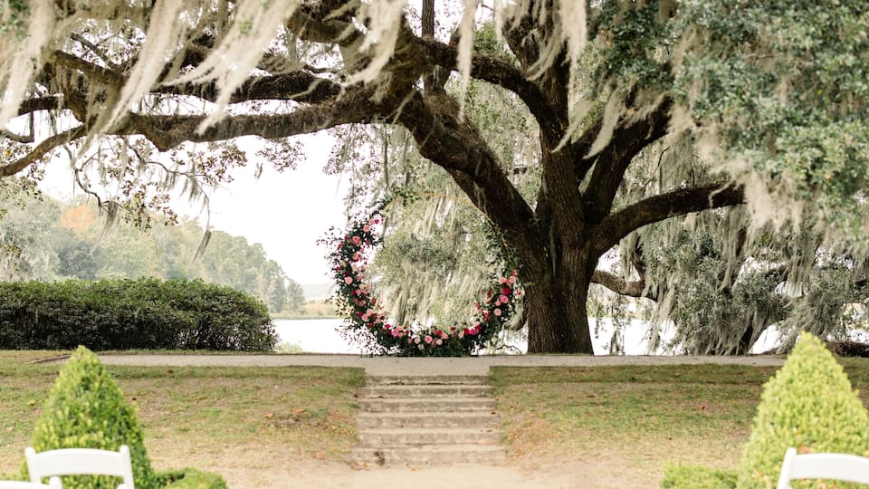 Outdoor wedding ceremony setup with a floral arch under oak tree