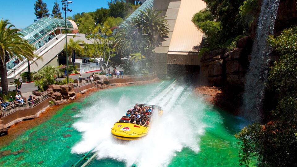 A water ride with a yellow boat, clear turquoise water, rocky terrain, palm trees, and a waterfall.
