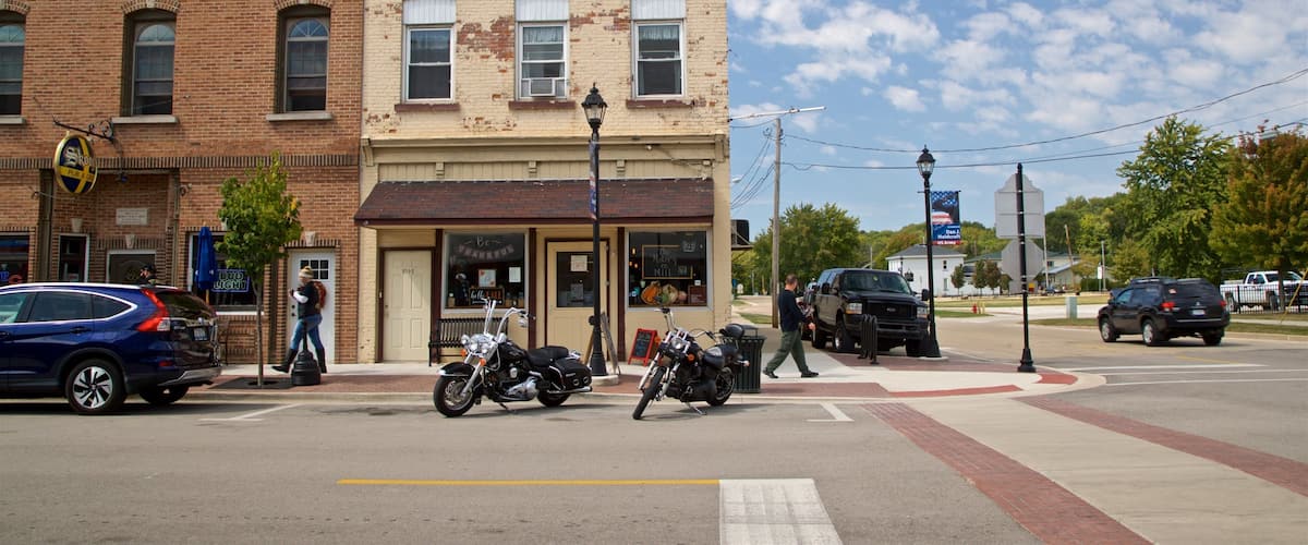 A street with a bakery, motorcycles parked on the sidewalk, and a blue car.