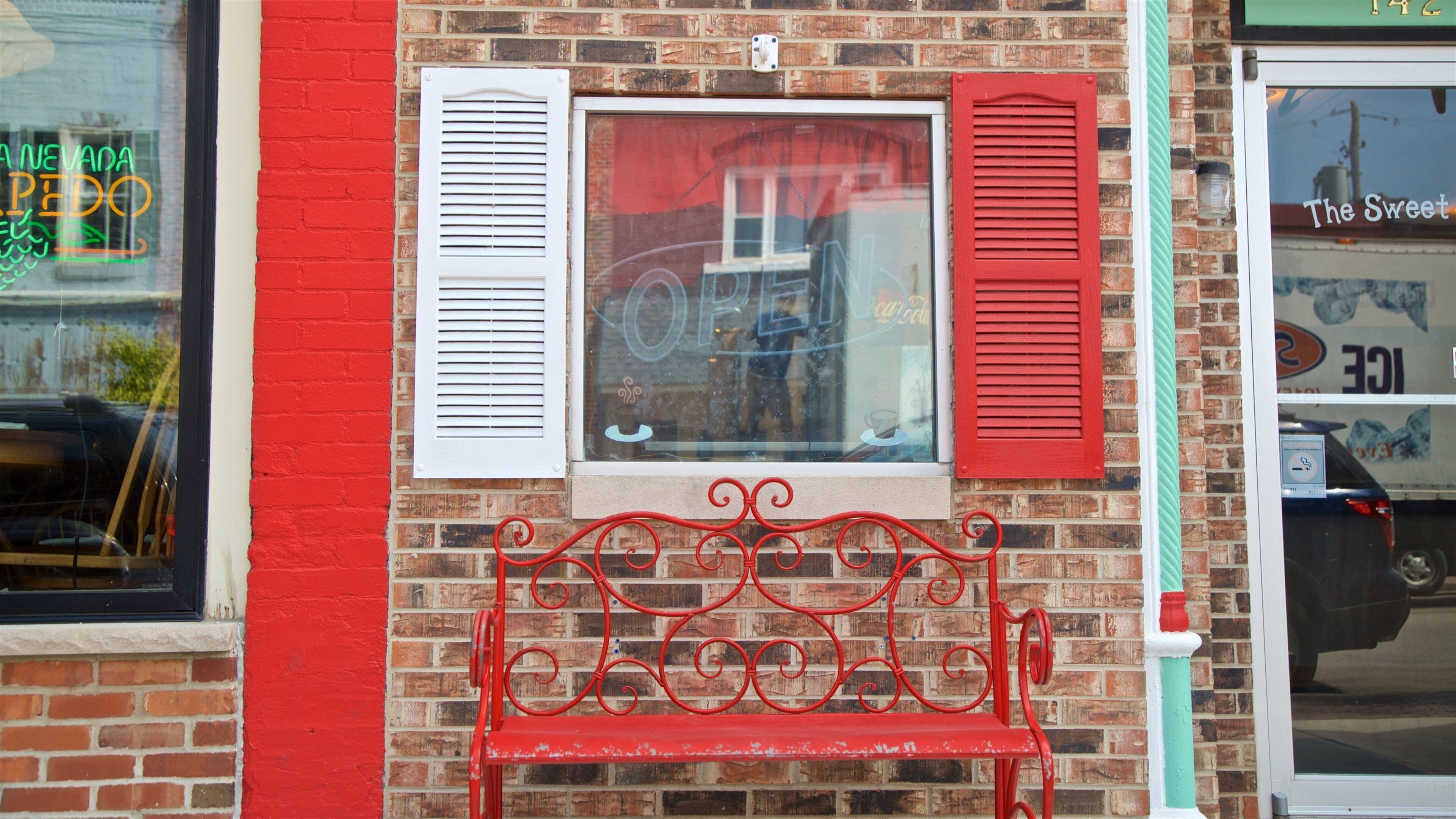 A red bench in front of a brick building with red and white shutters.