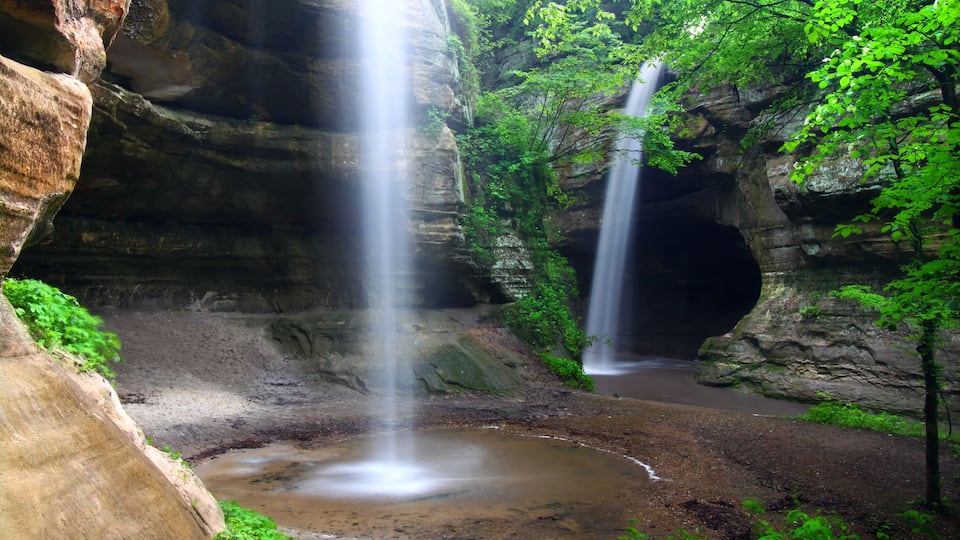 A waterfall cascading into a pool surrounded by rocky cliffs and lush greenery.