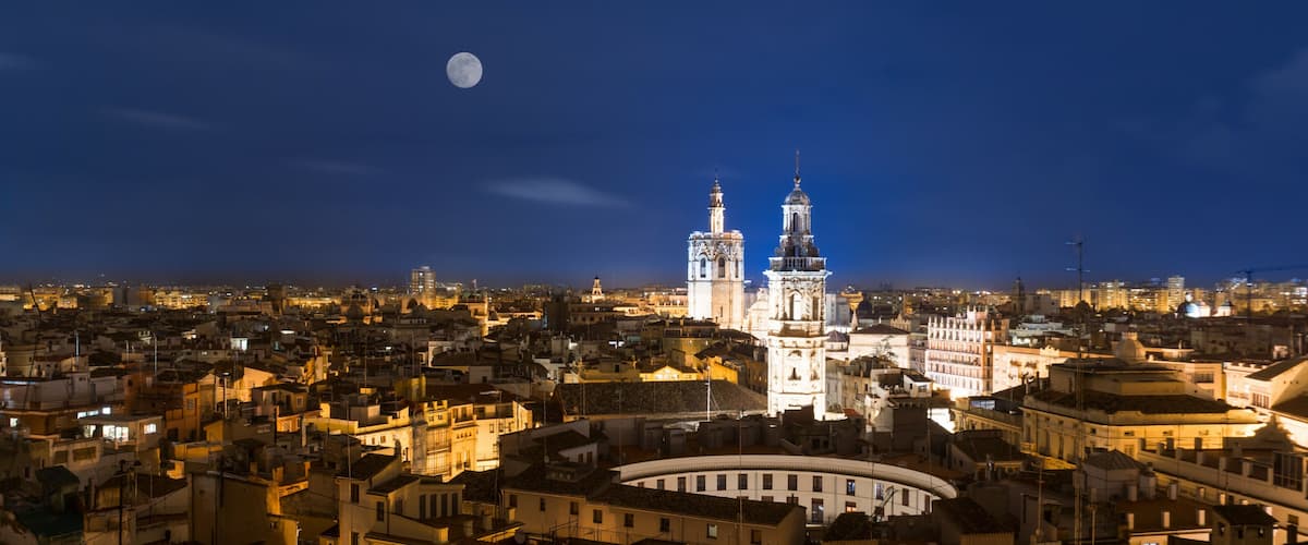 A cityscape at night with illuminated buildings and a prominent church with two towers.
