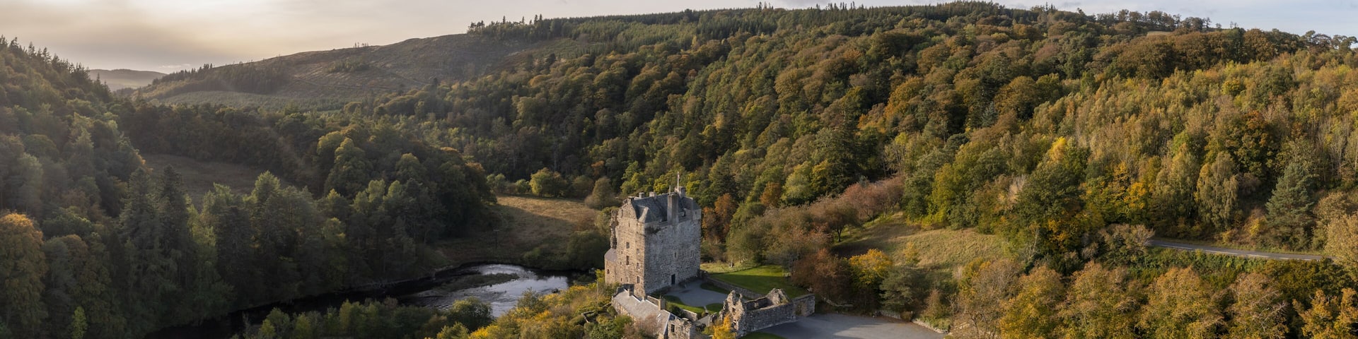 Aerial view of the historic Neidpath Castle standing proudly amidst the autumnal hues of the surrounding forest, where the River Tweed meanders serenely, Peebles, Scotland, United Kingdom.