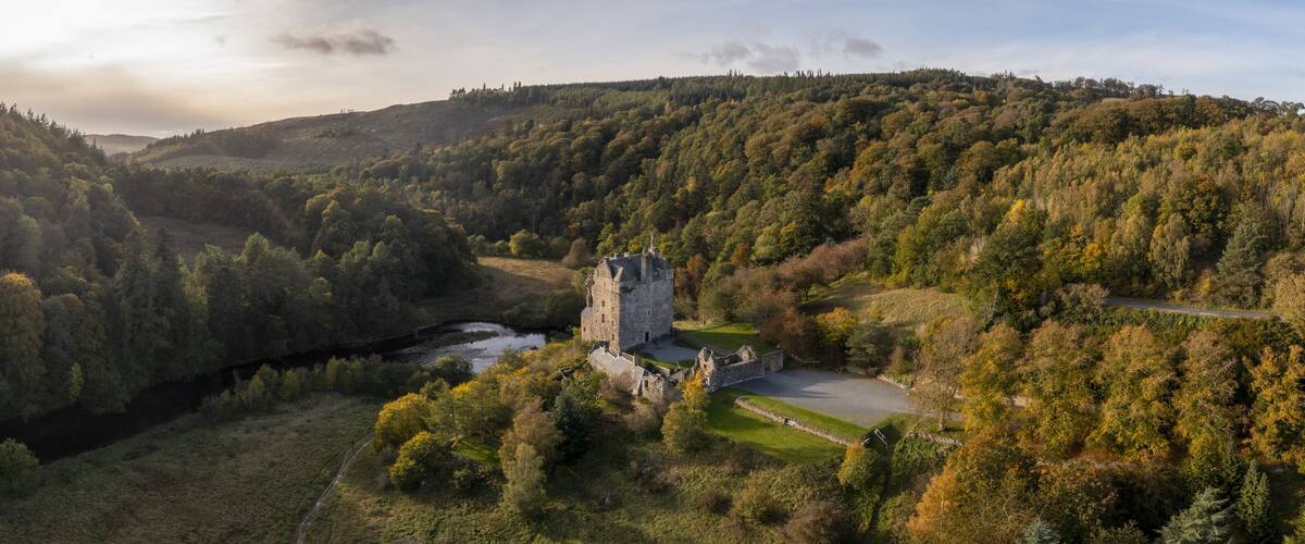 Aerial view of the historic Neidpath Castle standing proudly amidst the autumnal hues of the surrounding forest, where the River Tweed meanders serenely, Peebles, Scotland, United Kingdom.