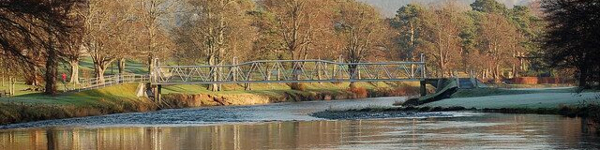 Un río con un puente, árboles y colinas al fondo.