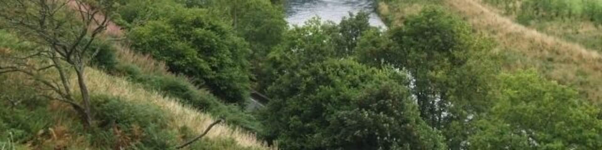 The Tweed near Cardrona. The A72 road is squeezed between the river and the steep bank on the left, with the line of an old railway and a golf course on the right.