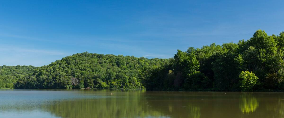 A calm lake with dense forested hills in the background.