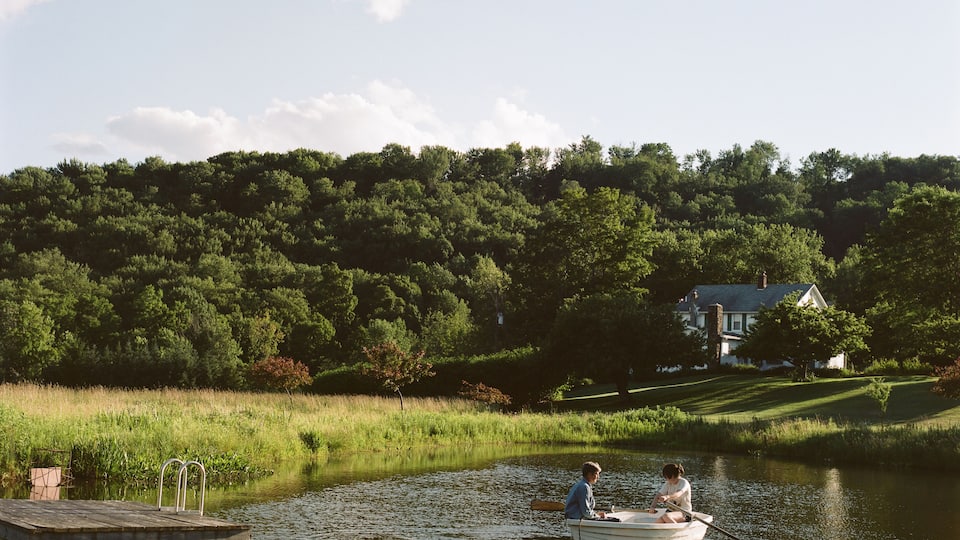 A calm lake with a dock and two people rowing a boat.