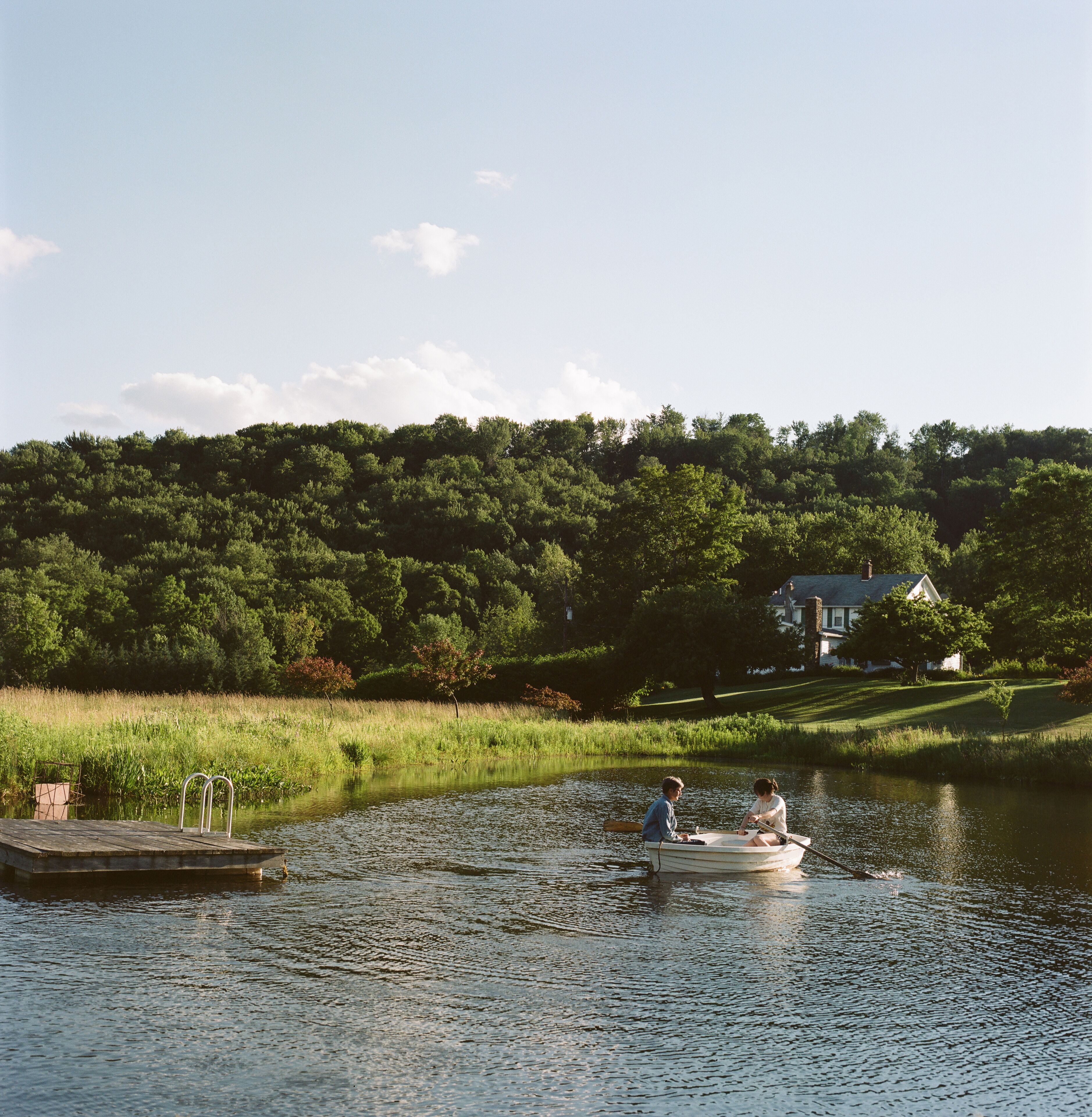 A calm lake with a dock and two people rowing a boat.