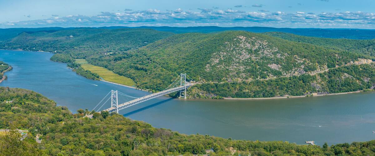 A suspension bridge over a river, surrounded by lush green hills.