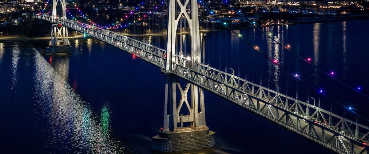 A nighttime view of a bridge with colorful lights reflecting on the water.