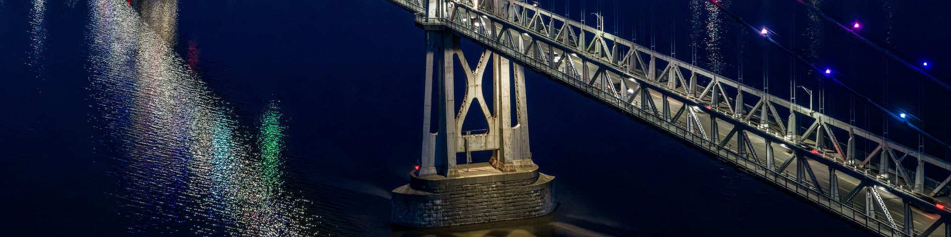 A nighttime view of a bridge with colorful lights reflecting on the water.