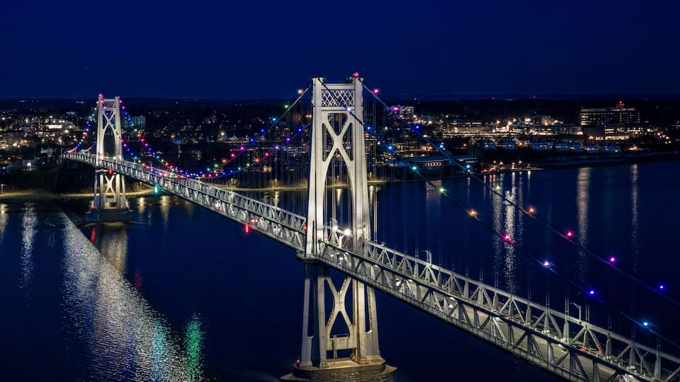 A nighttime view of a bridge with colorful lights reflecting on the water.