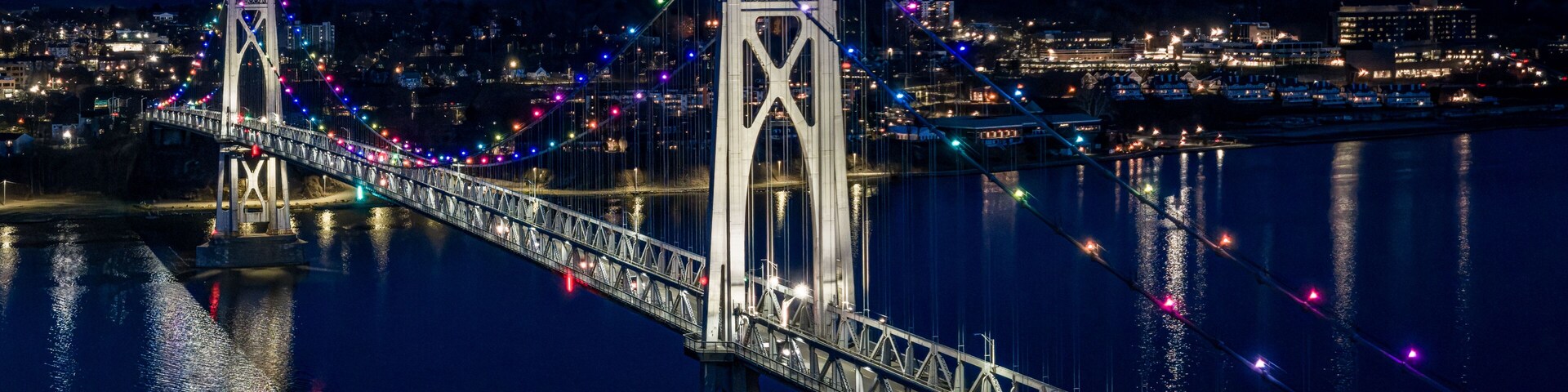 Ein Nachtblick auf eine Brücke, deren farbige Lichter sich im Wasser spiegeln.