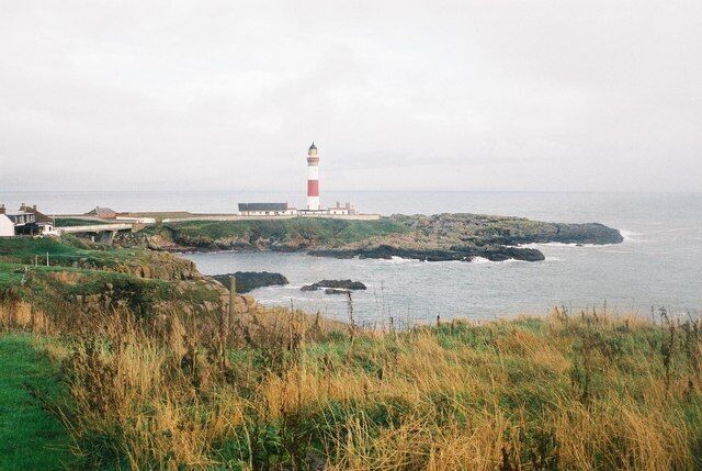 A lighthouse on a rocky coastline with grassy foreground and a cloudy sky.