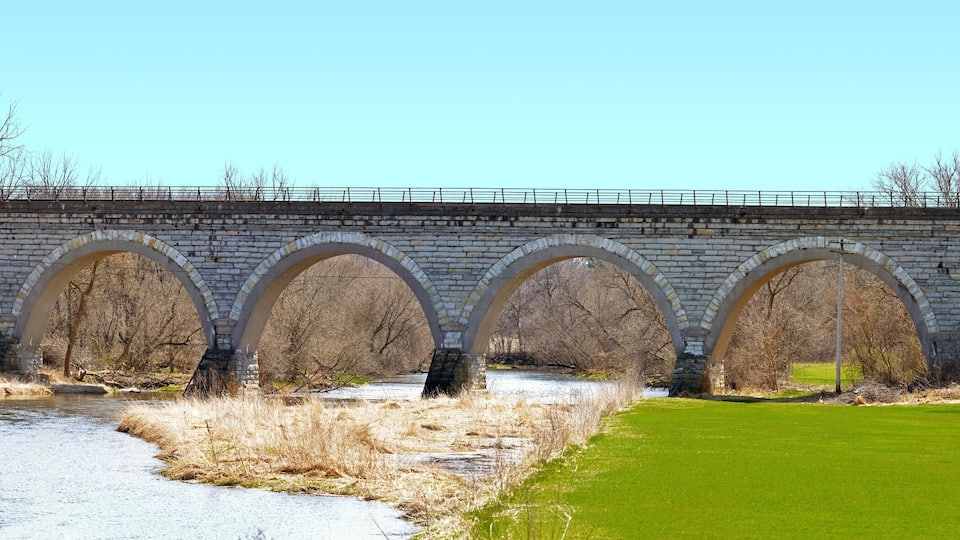 A stone bridge with multiple arches over a river, surrounded by trees and grassy areas.