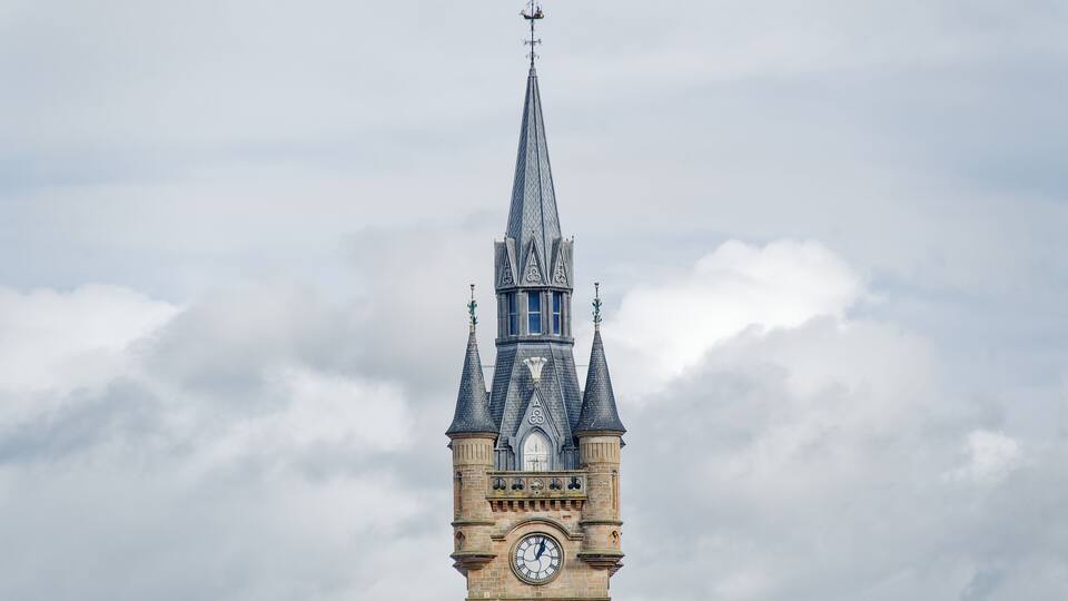A clock tower with a pointed spire and a weather vane.