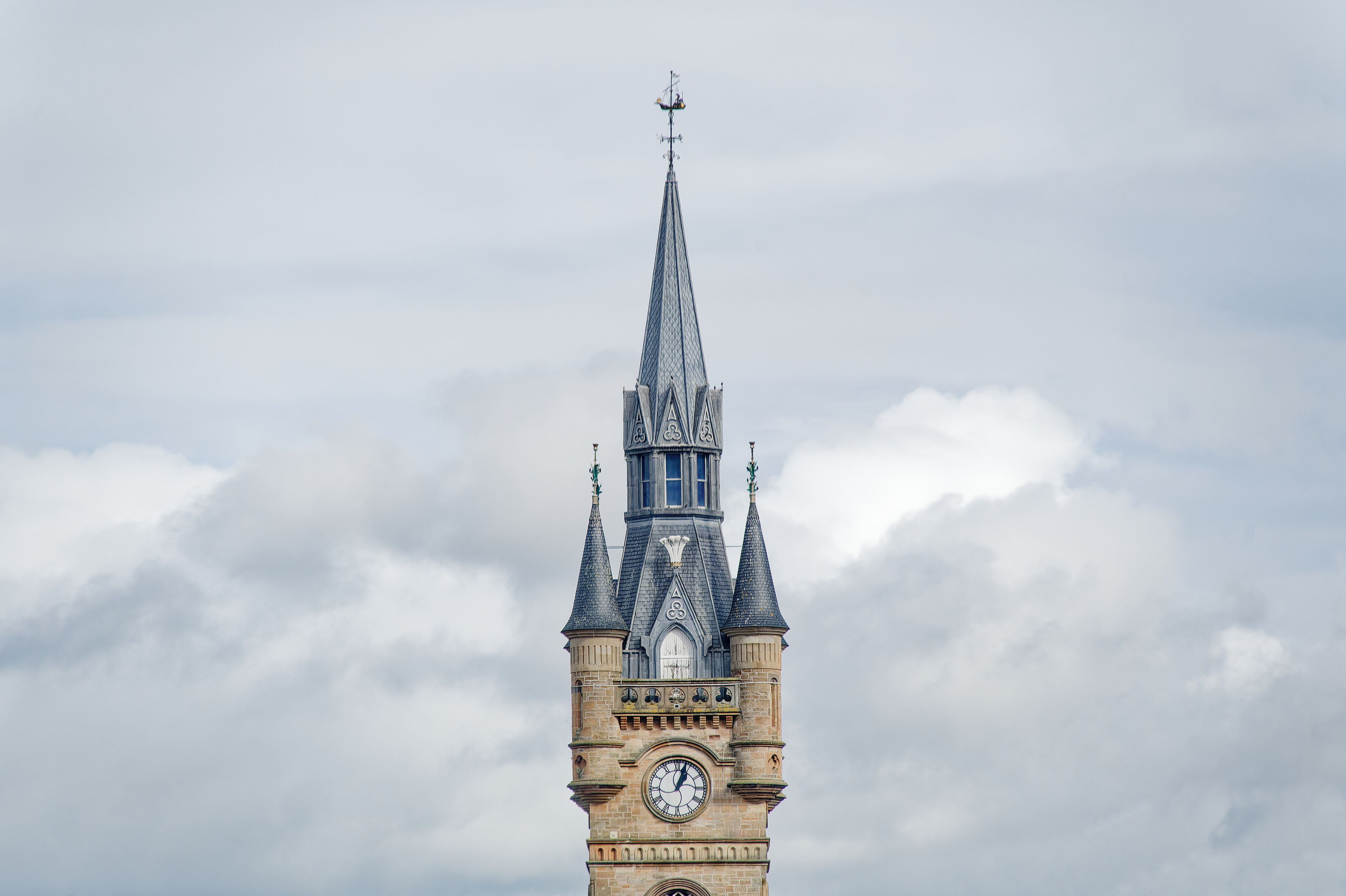 A clock tower with a pointed spire and a weather vane.