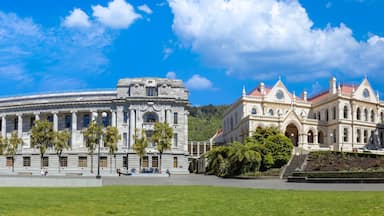A large, historic building with classical architecture, surrounded by a well-maintained park and a modern skyscraper.
