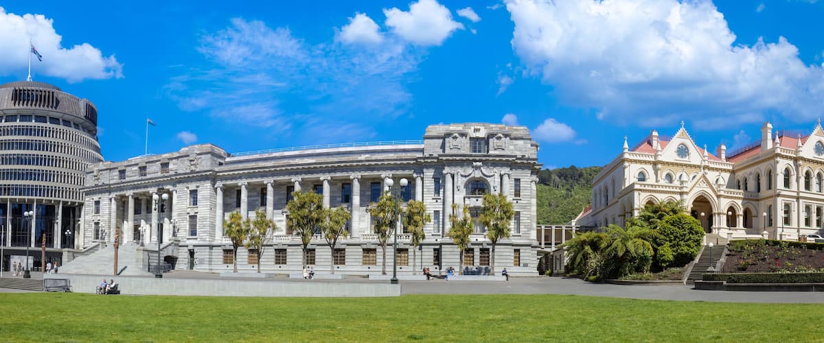 A large, historic building with classical architecture, surrounded by a well-maintained park and a modern skyscraper.