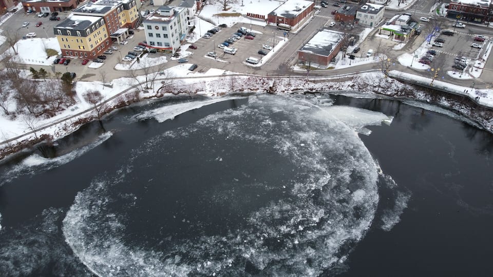 A frozen river with a bridge crossing over it, surrounded by buildings and parked cars.
